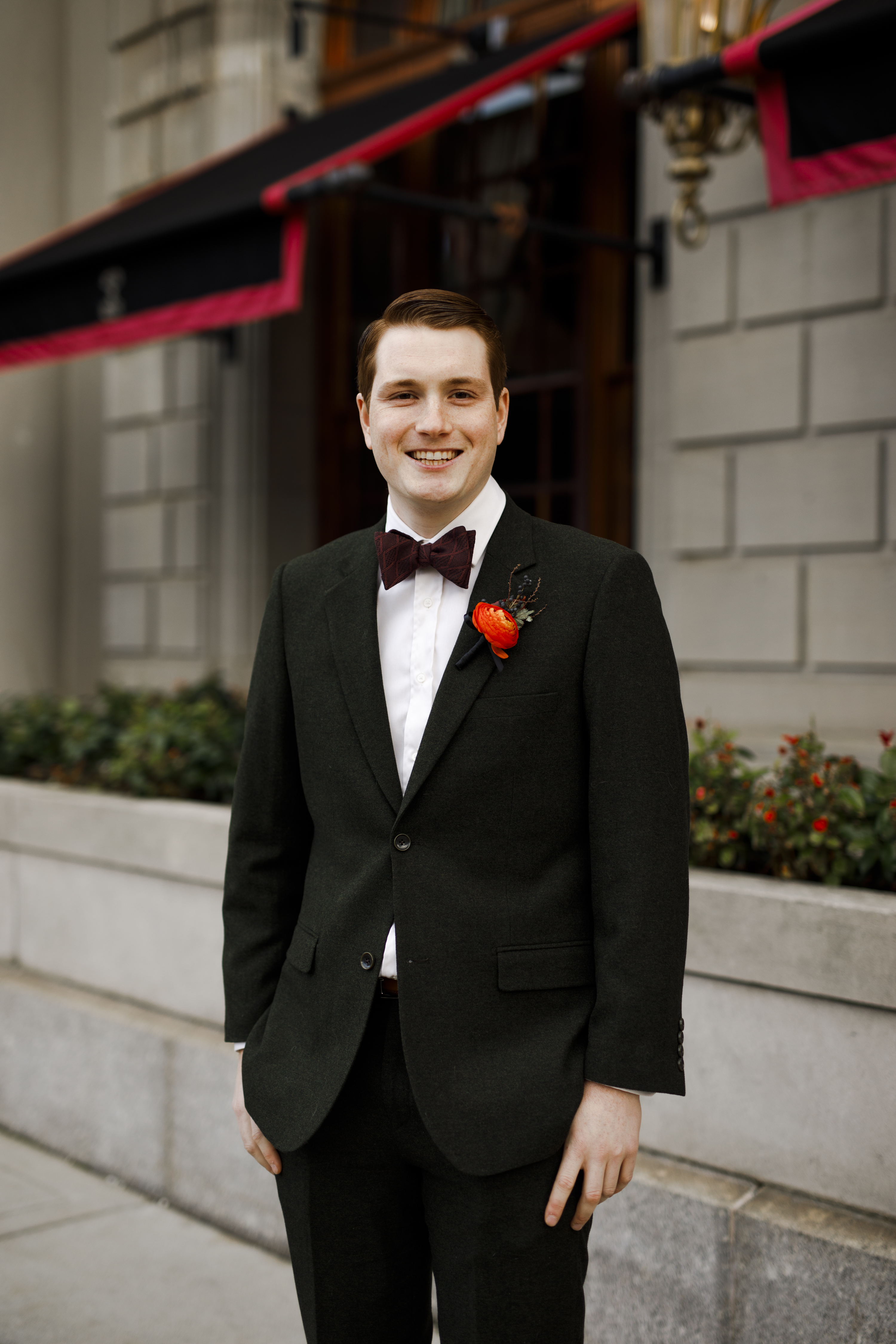Alex smiling outdoors in black tuxedo with boutonniere